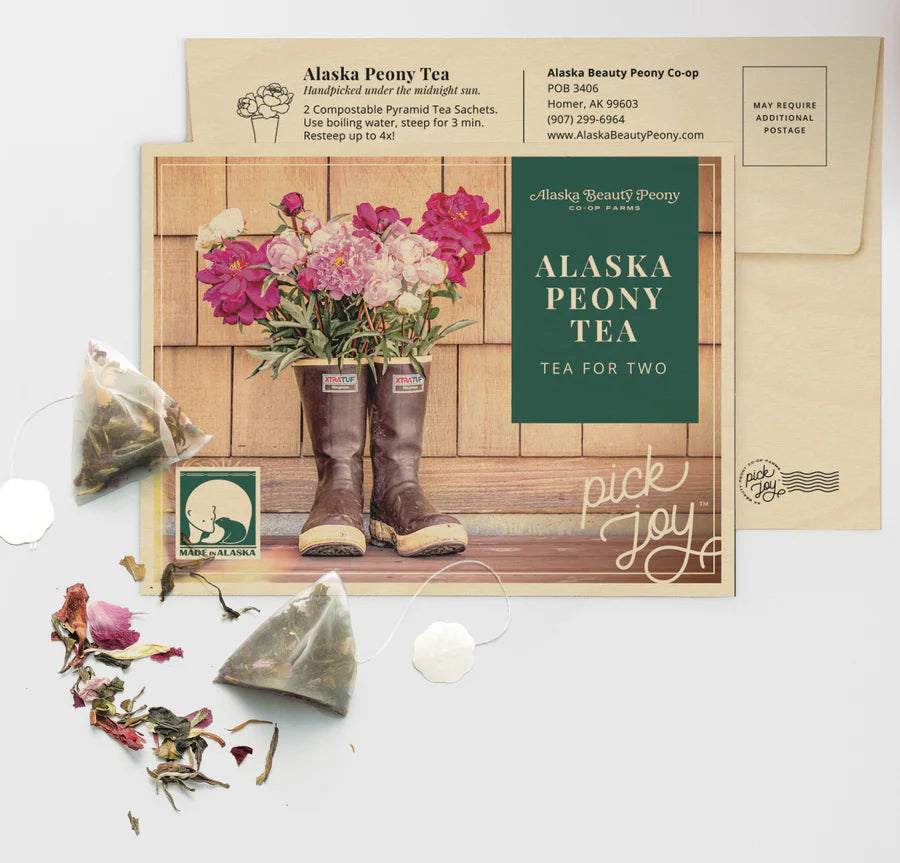 Product image for Peony Tea for Two, featuring two pyramid tea sachets, dried peony petals, and a card with 'Alaska Peony Tea' branding and a pickup location address.
