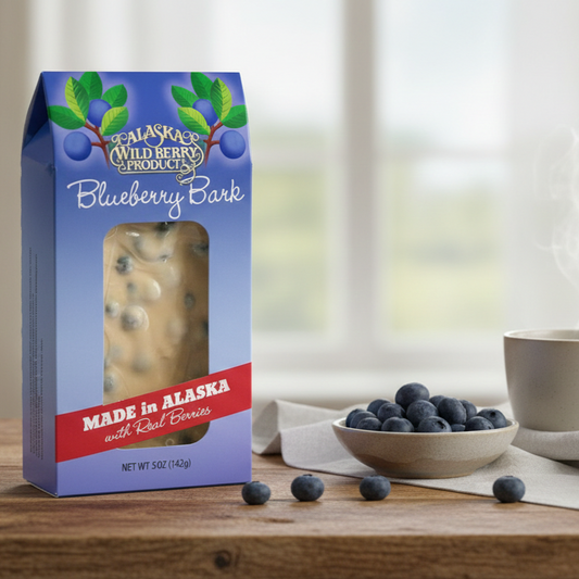 Blueberry Bark box with visible blueberry-studded candy, surrounded by fresh blueberries, a steaming beverage, and a napkin on a wooden tabletop.