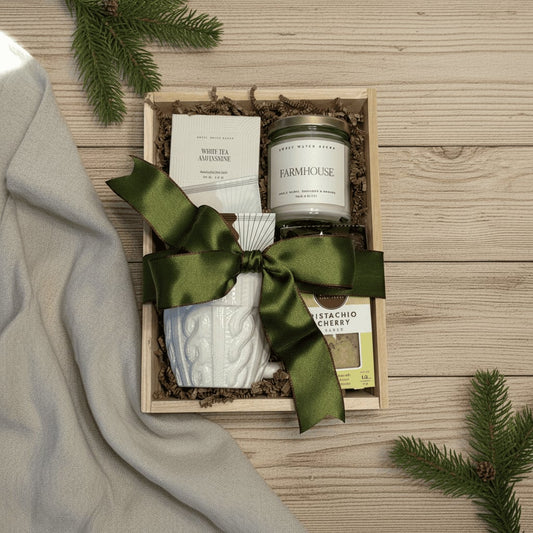 Gift set with a bath bomb, candle, mug, cookie, and tea in a wooden box on a wooden surface.