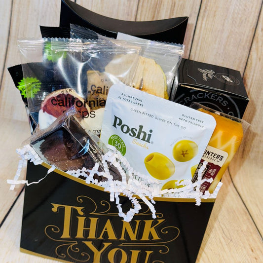 A gift basket with a variety of gourmet treats including smoked salmon, artisan crackers, gourmet cheese, handpicked olives, roasted pistachios, premium coffee, dried fruits, and chocolates, packaged in a black box with a gold ribbon and the text 'THANK YOU' displayed.