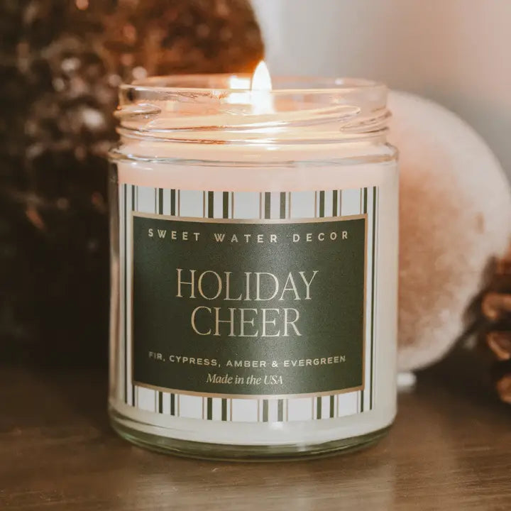 Candle in a jar labeled 'Holiday Cheer' by Sweet Water Decor on a wooden surface.
