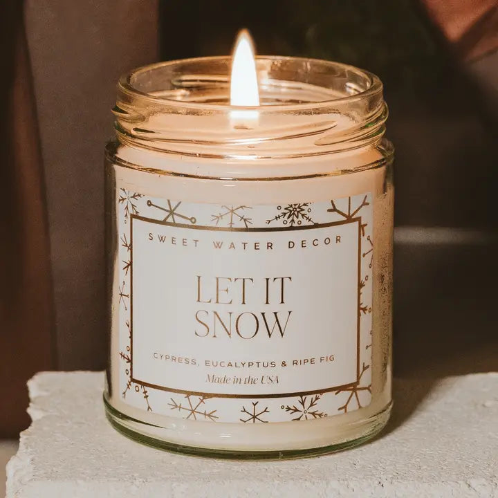 Candle in a jar with 'Let It Snow' label on a neutral background