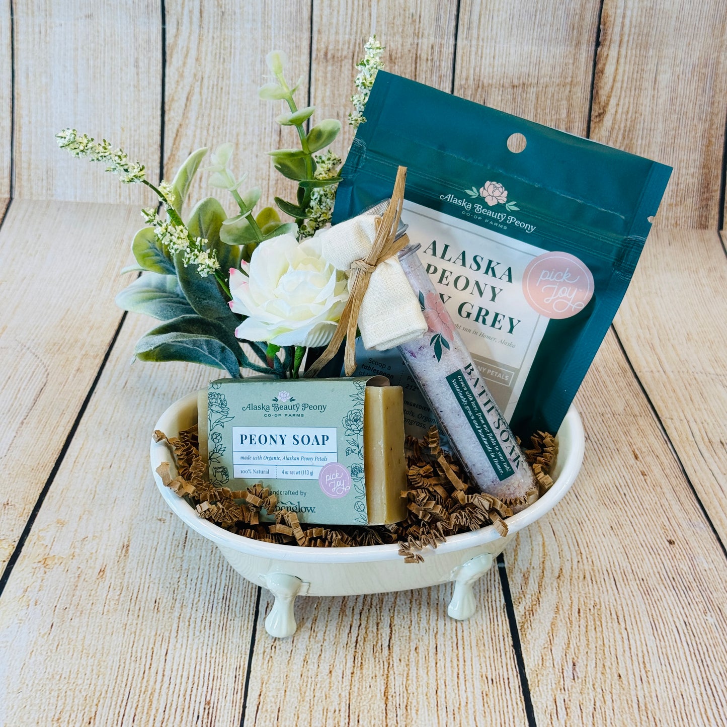 A gift basket arranged in a mini metal claw-foot bathtub with a bar of soap, a bottle of body wash, and a package of bath salts, all labeled 'Alaska Beauty Peony'.