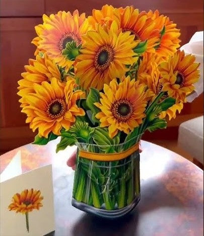Pop-up Flower Bouquets: A clear glass vase with yellow-orange daisy-like blooms and a matching greeting card, perfect for brightening rooms and gifting occasions.