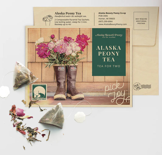 Product image for Peony Tea for Two, featuring two pyramid tea sachets, dried peony petals, and a card with 'Alaska Peony Tea' branding and a pickup location address.