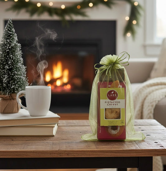Artisan Bites Gift Set with Pistachio Cherry cookies in organza bag, placed on a cozy holiday table near a steaming mug and mini evergreen.