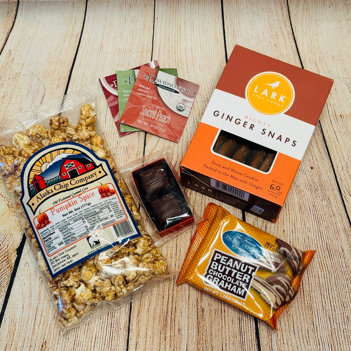 Assorted snacks including pumpkin spice popcorn, chocolate bars, and ginger snaps on a wooden surface.