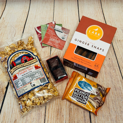 Assorted snacks including pumpkin spice popcorn, chocolate bars, and ginger snaps on a wooden surface.
