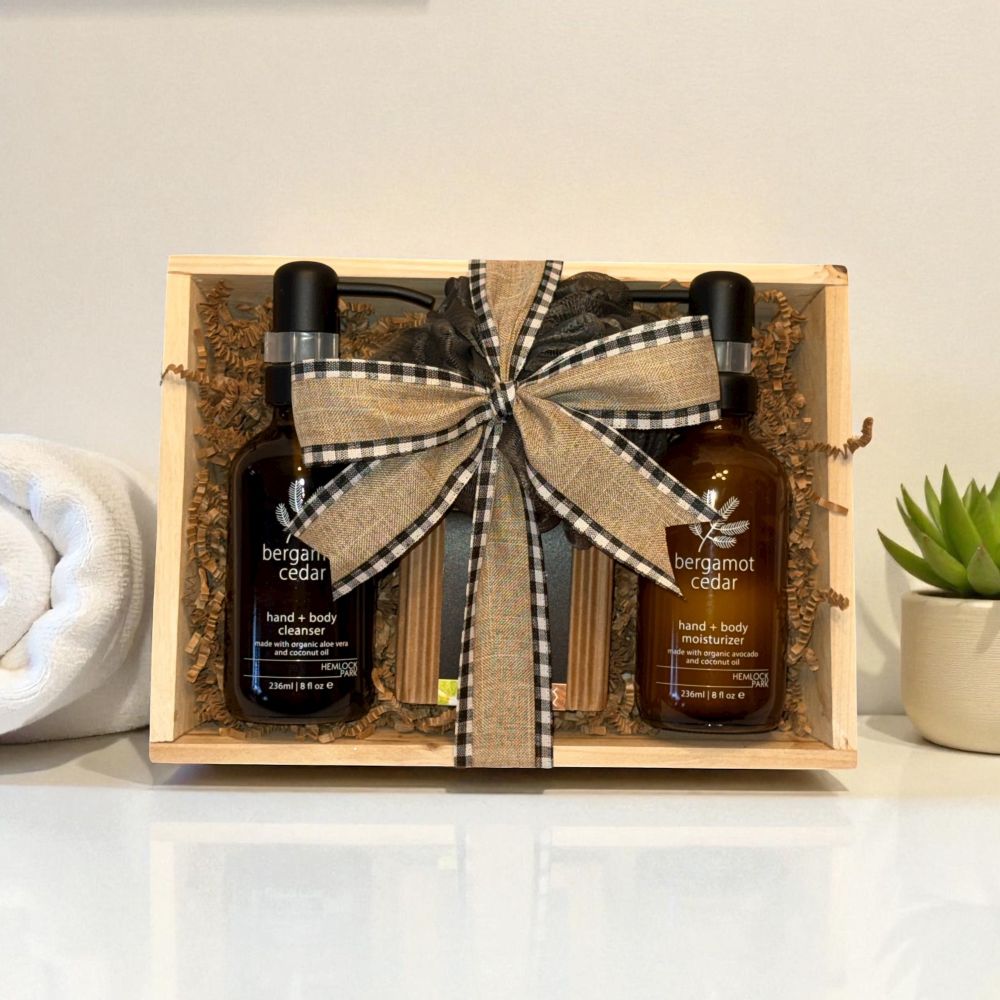 Gift set with two bottles of bergamot cedar product in a wooden crate with a bow, on a light background.