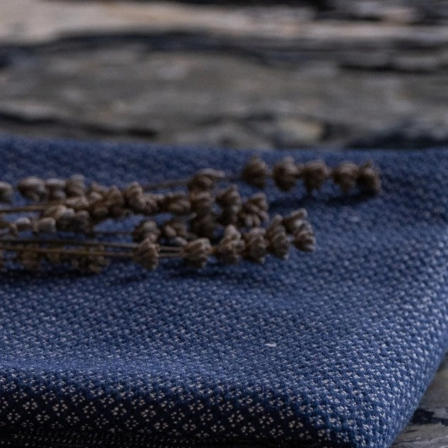 A  blue-colored Turkish throw blanket laying flat with a bundle of dried lavender flowers tied with a string on top, placed on a marble surface.