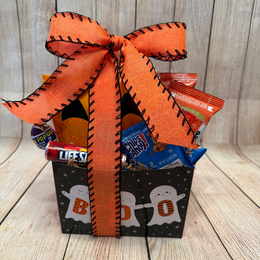 Halloween-themed gift box with candy, cookies, lollipops and an orange ribbon on a wooden surface