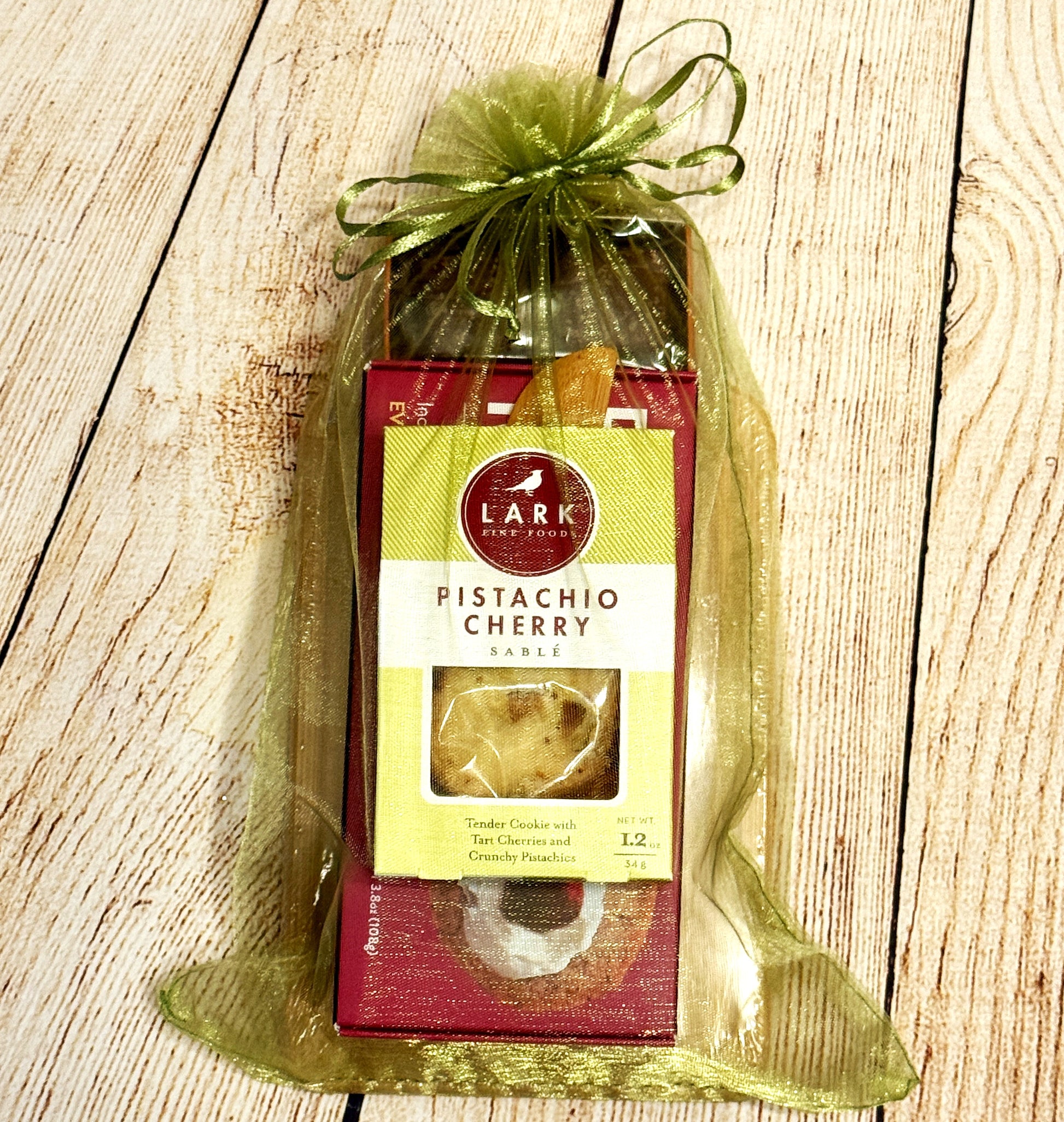 Packaged pistachio cherry cookies with Crackerology Snackables a green ribbon on a wooden surface