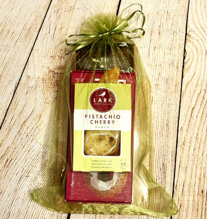 Packaged pistachio cherry cookies with Crackerology Snackables a green ribbon on a wooden surface