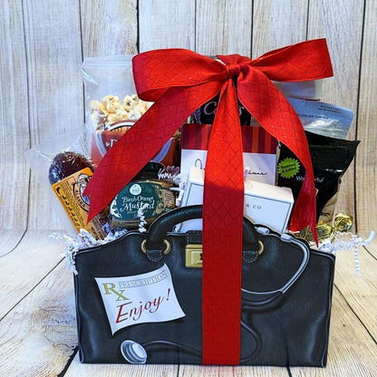 A gift basket with an assortment of food items such as crackers, cheese spread, sausage, mustard, olives, tea, cookies, and pistachio cheese straws, packaged in a decorative black bag with a red ribbon.