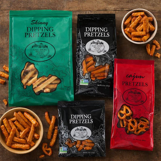 Assorted packages of pretzels including 'Skinny Dipping Pretzels', 'Dipping Pretzels', and 'Cajun Pretzels' on a wooden surface.