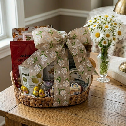 Easter Delights Gift Basket on a table with gourmet snacks, foil-wrapped chocolates, a daisy ribbon, and a vase of daisies nearby.