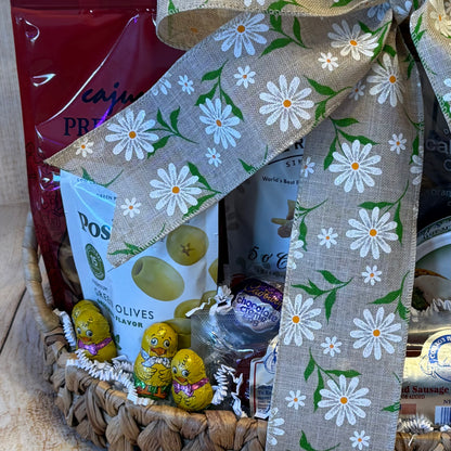 Easter Delights Gift Basket with savory olives, sausage, nuts, crackers, and sweet chocolate chicks, all adorned with a burlap ribbon featuring white daisies.