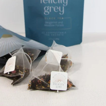Felicity Grey tea set with pyramid sachets, featuring black tea blend with bergamot, mandarin peels, and floral elements, in a branded pouch.