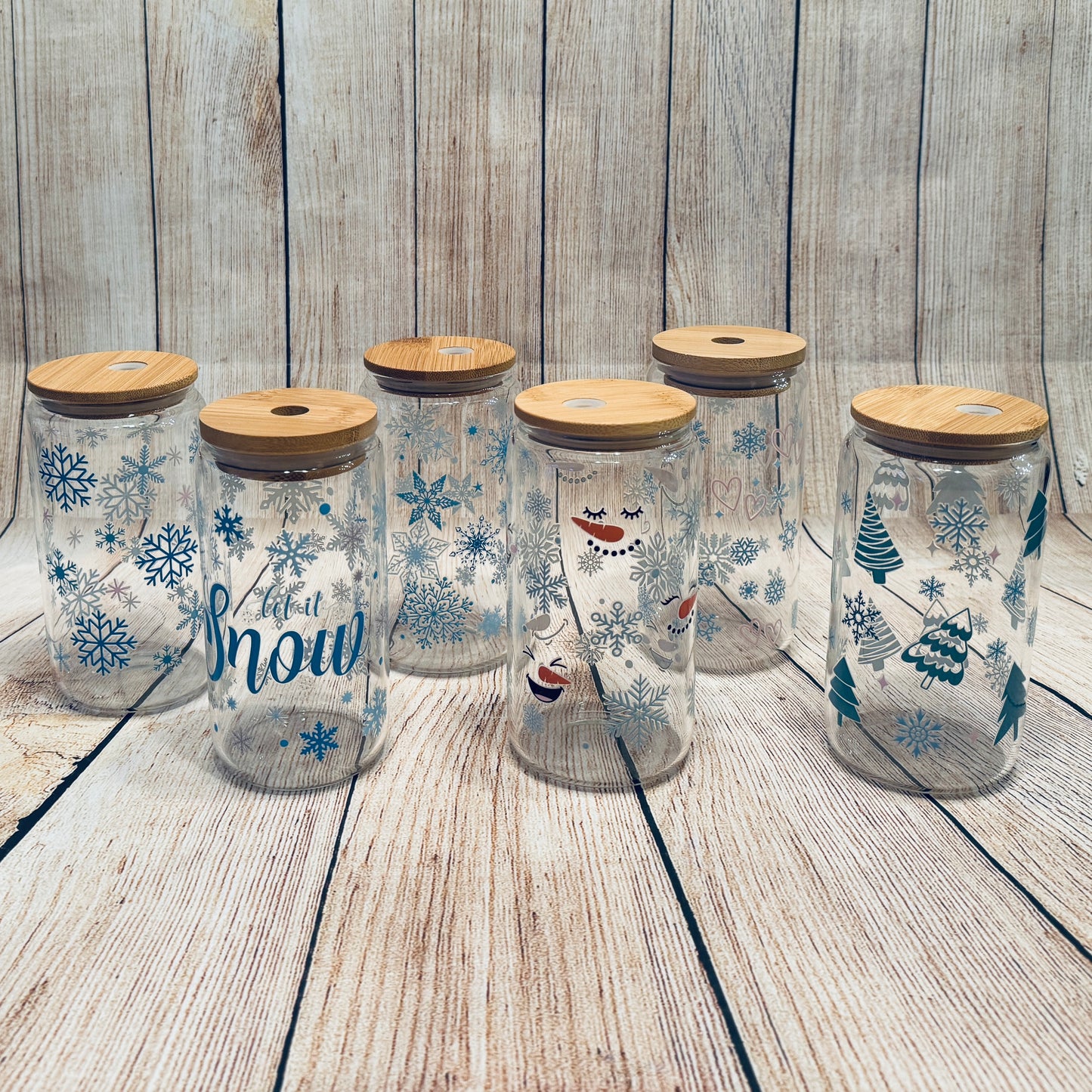 Glass tumblers with various winter-themed graphics, including snowflakes and Christmas trees, each with a bamboo lid.