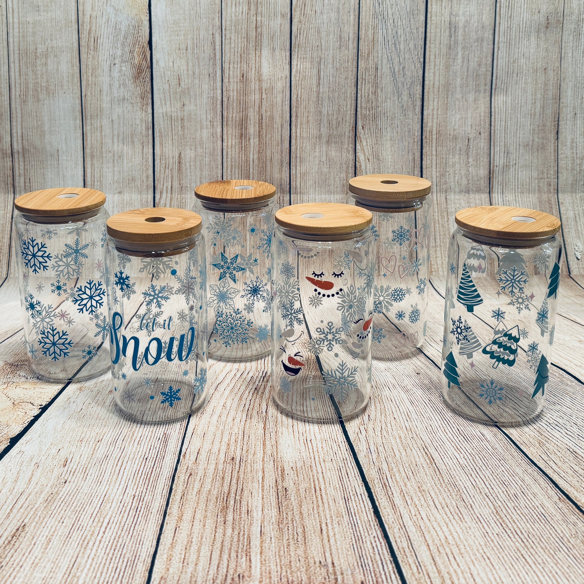 Glass tumblers with various winter-themed graphics, including snowflakes and Christmas trees, each with a bamboo lid.