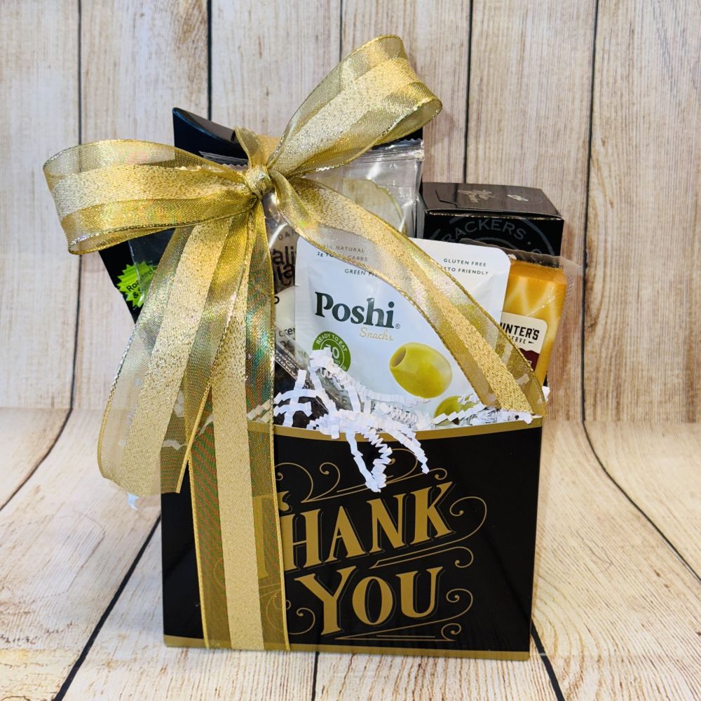 A gift basket with a variety of gourmet treats including smoked salmon, artisan crackers, gourmet cheese, handpicked olives, roasted pistachios, premium coffee, dried fruits, and chocolates, packaged in a black box with a gold ribbon and the text 'THANK YOU' displayed.
