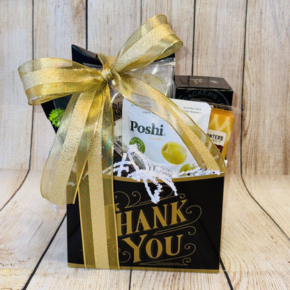 A gift basket with a variety of gourmet treats including smoked salmon, artisan crackers, gourmet cheese, handpicked olives, roasted pistachios, premium coffee, dried fruits, and chocolates, packaged in a black box with a gold ribbon and the text 'THANK YOU' displayed.