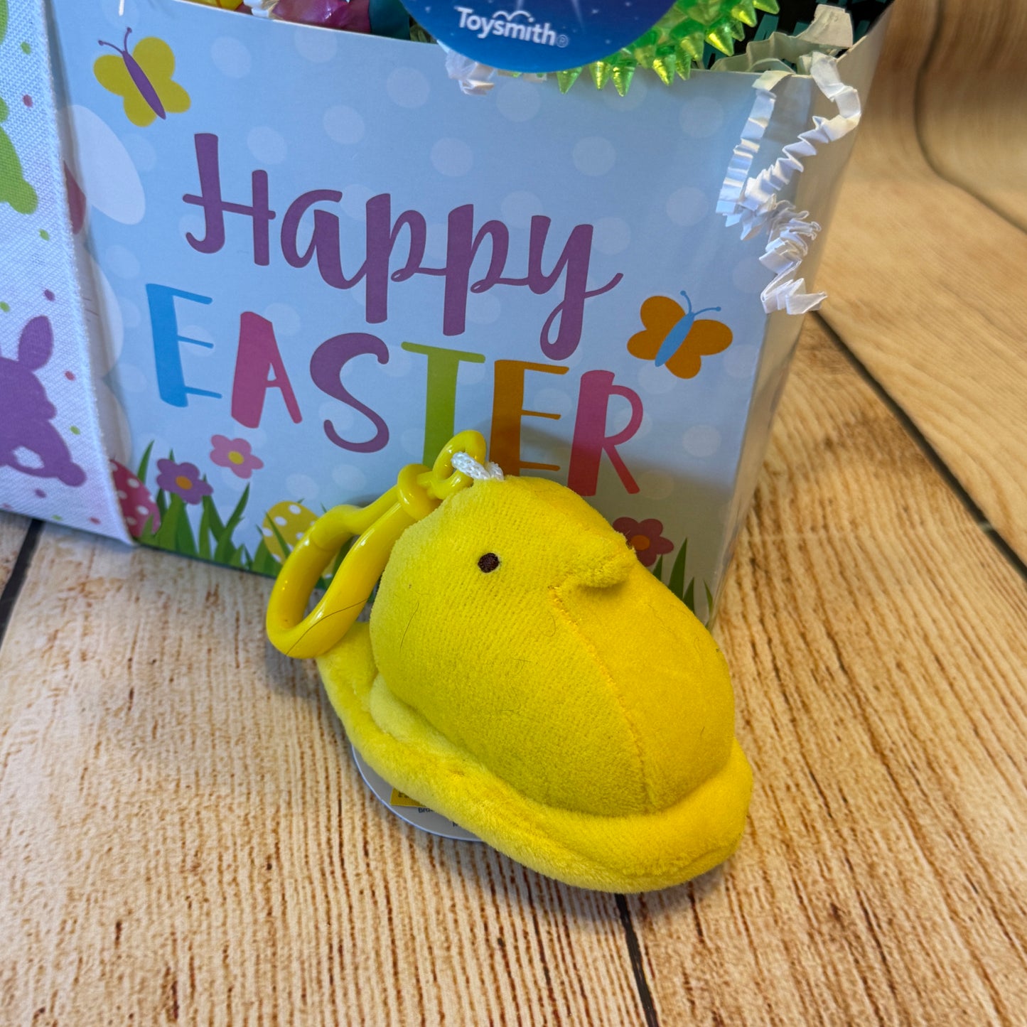 Pastel Happy Easter gift bag with a butterfly design and plush chick key-chain, featuring festive treats and toys from the Happy Easter Gift Basket.