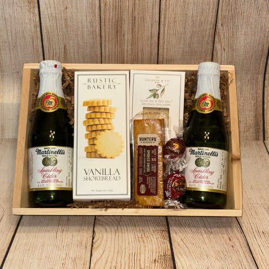 Gift basket with Martinellis sparkling cider, vanilla shortbread, and other items on a wooden surface.
