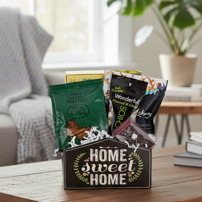 Home Sweet Home Gift Basket with pretzels, pistachios, dried fruit, a chocolate bar, and white paper shred in a cozy setting.