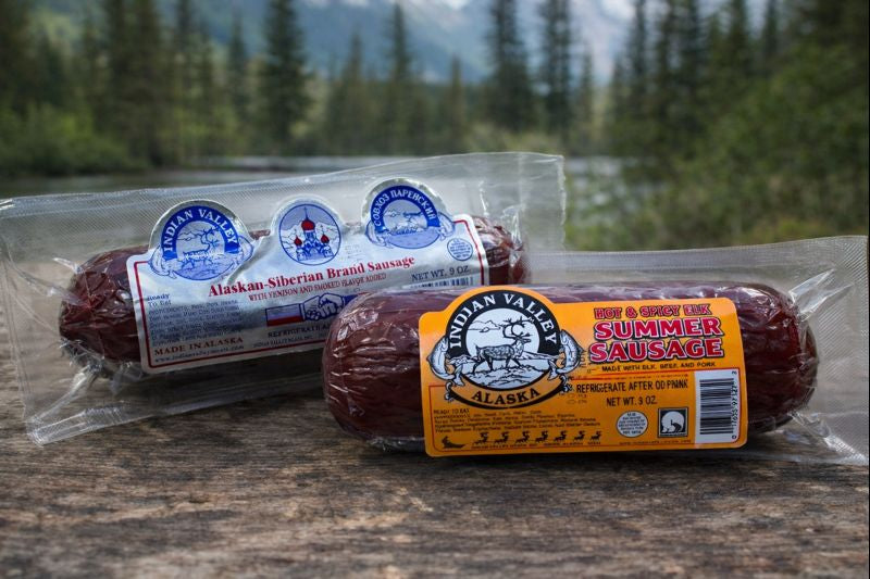 Two packages of Indian Valley Alaska summer sausage on a wooden surface with a natural background.