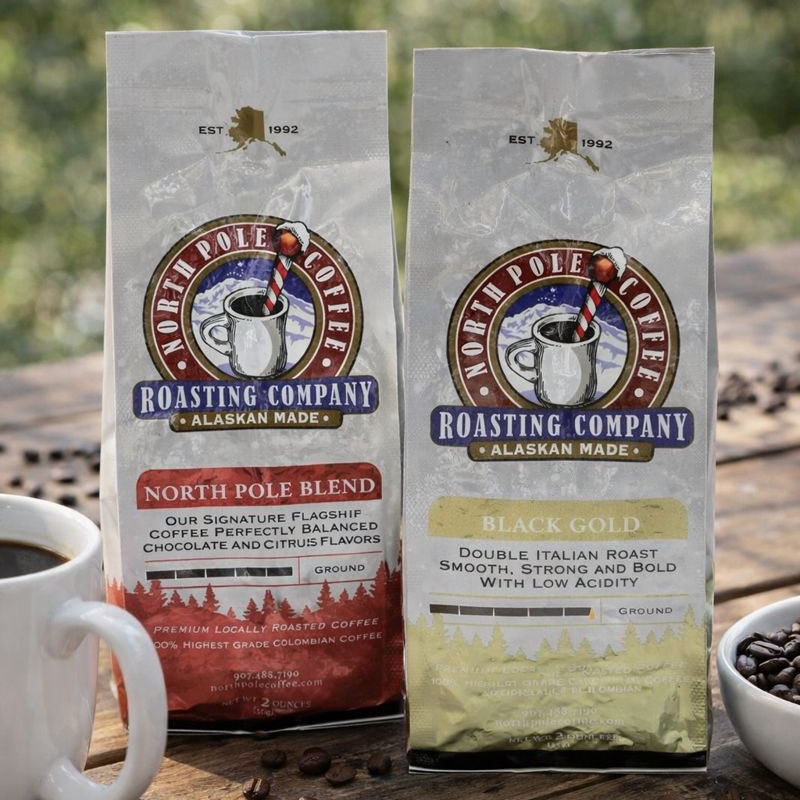 Two packages of North Pole Coffee Roasting Company coffee on a wooden surface with a cup and bowl of coffee beans.
