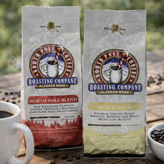 Two packages of North Pole Coffee Roasting Company coffee on a wooden surface with a cup and bowl of coffee beans.