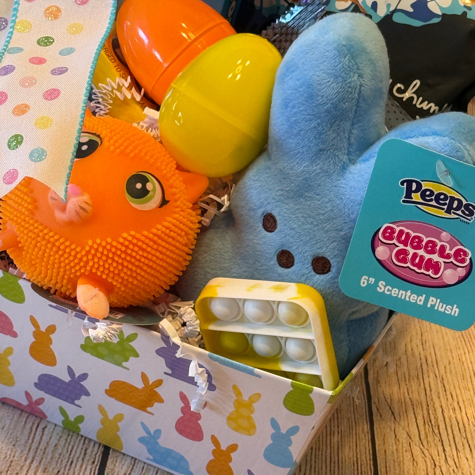 Peep, Peep Easter Basket - Blue: Easter-themed box with a plush bunny, Easter eggs, squishy cat toy, and fidget toy, all atop shredded paper.