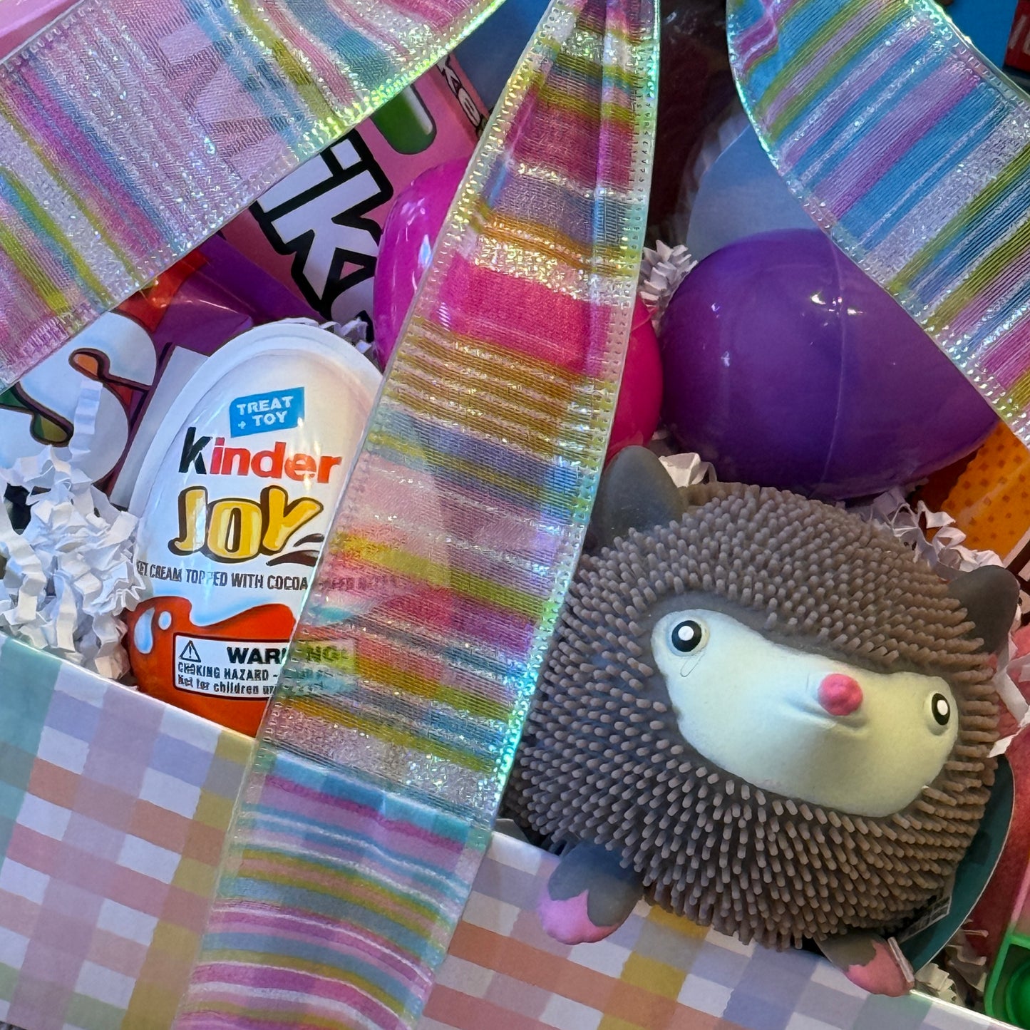Peep Peep Easter Basket - Pink features a Kinder Joy egg, Skittles, plush hedgehog toy, and surprise eggs, tied with a pastel striped ribbon.