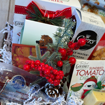 Assorted food items including a box of cookies, a jar of jelly, and a package of sundried tomato dip mix, with decorative elements like berries and pine cones.