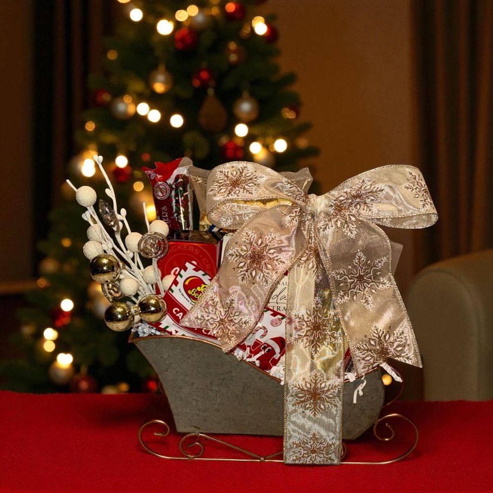 Decorative gift basket with a large bow in front of a Christmas tree.