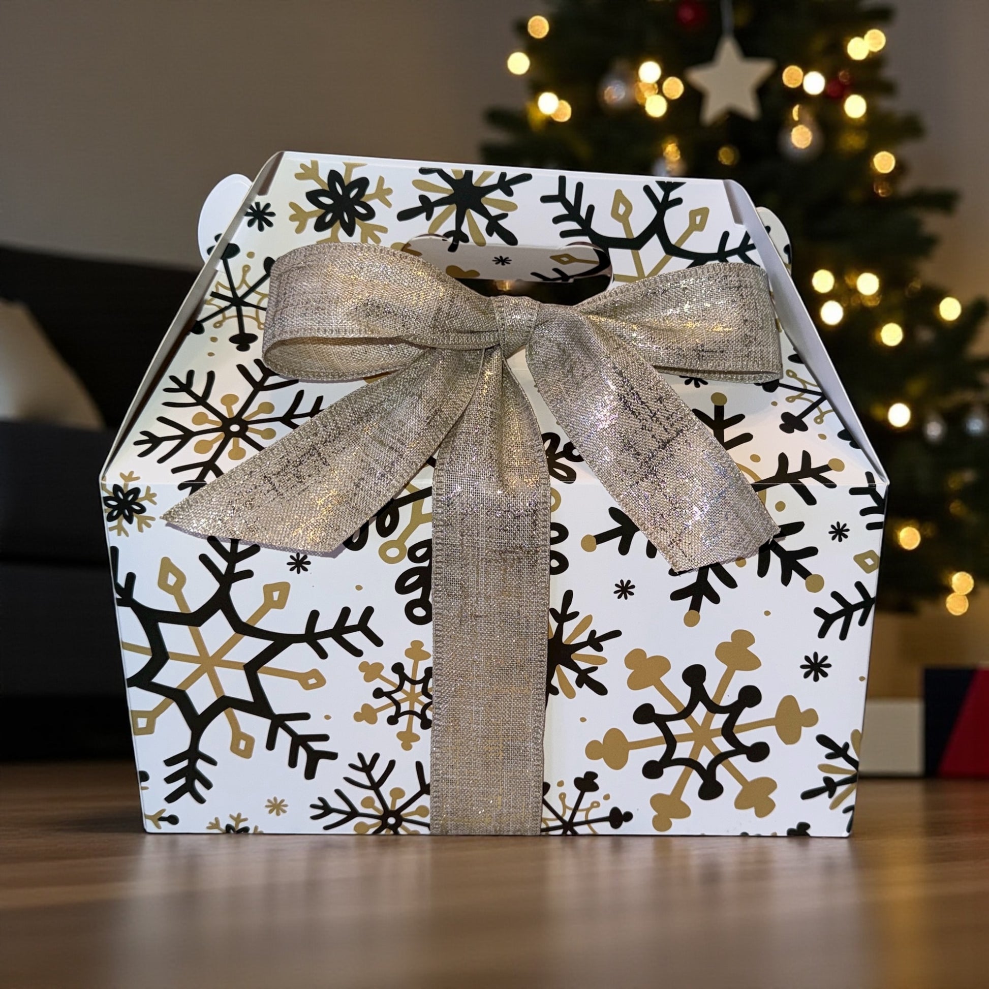 Gift box with snowflake pattern and gold ribbon in front of a Christmas tree