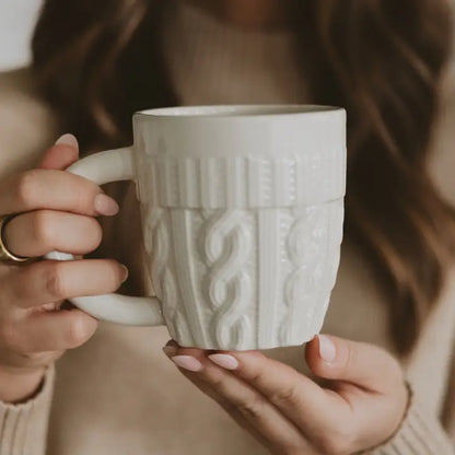 Person holding a textured white mug with a blurred background