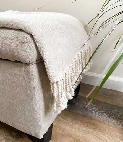A beige textured blanket draped over a chair with a plant in the corner 