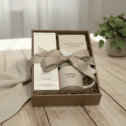 Gift set with mug, diffuser, and journal in a box on a wooden surface.