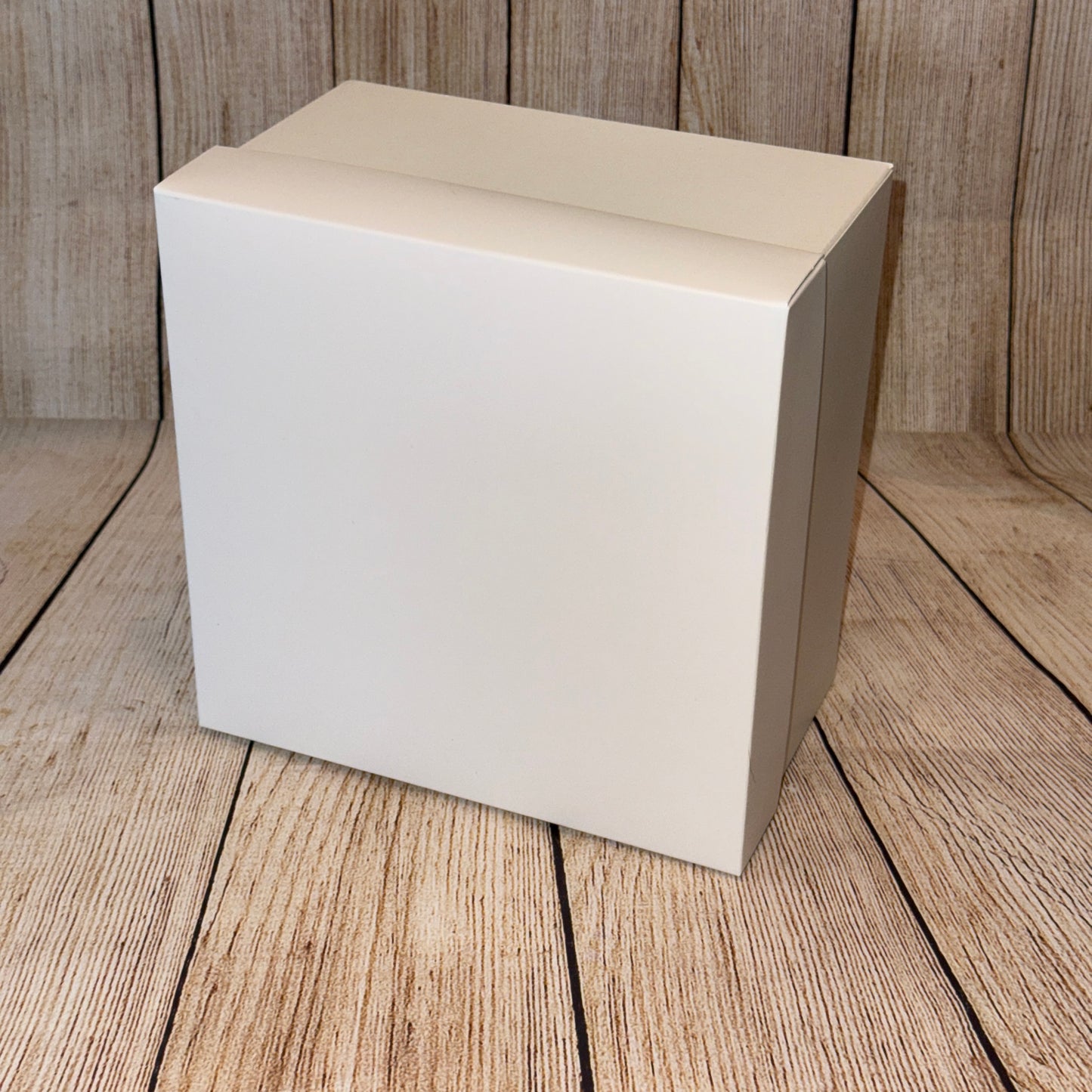 A white square gift box with a lid, placed on a wooden surface.
