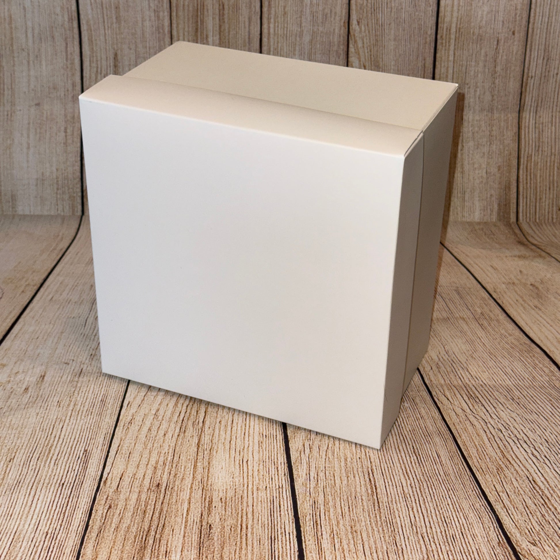 A white square gift box with a lid, placed on a wooden surface.