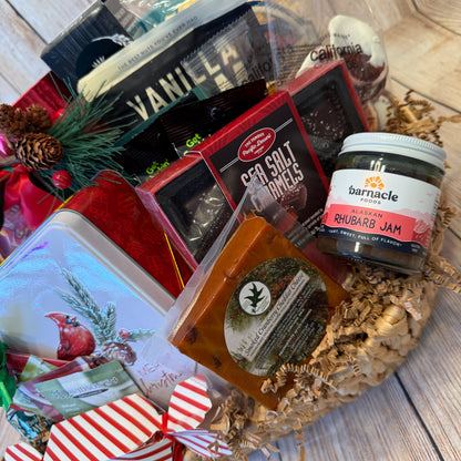 Assorted food items including a jar of rhubarb jam, sea salt caramel, and other packaged goods on a woven mat.