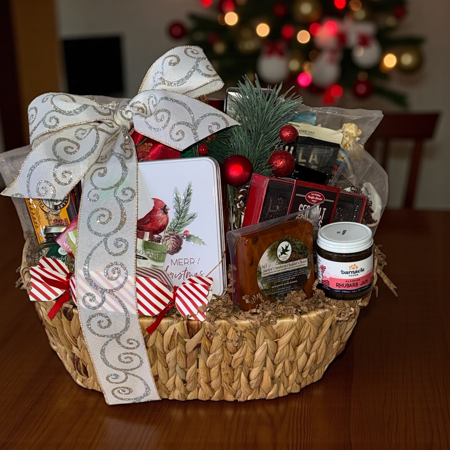 Gift basket with decorative bow on a wooden table in front of a Christmas tree.