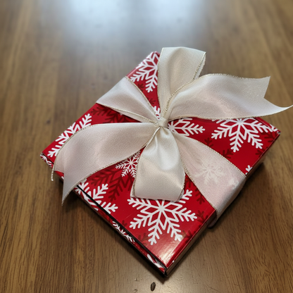 Red gift box with white snowflake pattern and a white ribbon on a wooden surface