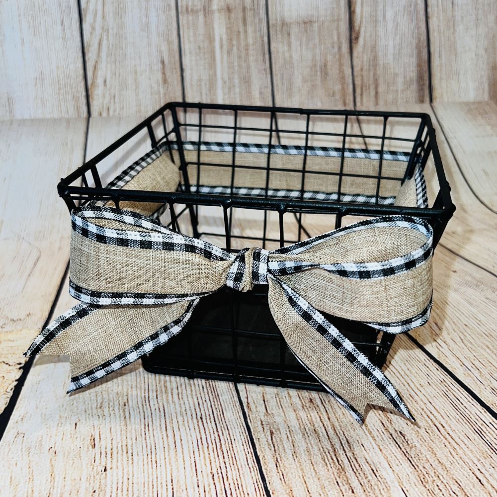 A black metal basket with a wood bottom and a beige checkered ribbon, displayed on a wooden surface.